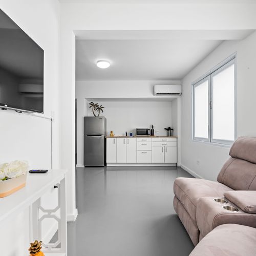 Our modern studio apartment offers a perfect blend of comfort and style, with a cozy beige sofa, chic white furnishings, and a fully-equipped kitchenette.