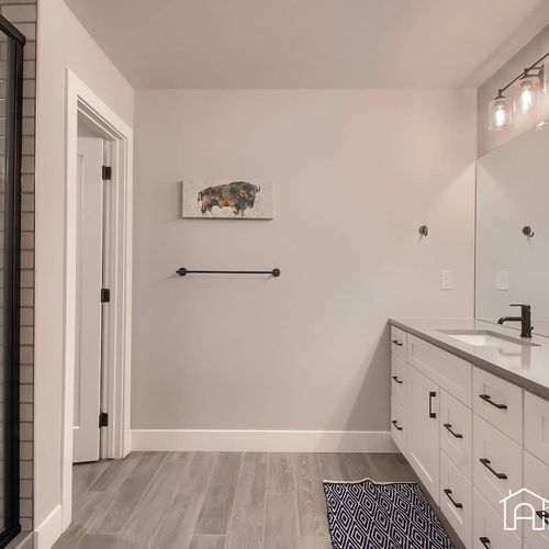 - modern bathroom with a wide dual sink vanity and sleek matte black fixtures
- wood look flooring and accent rug bring warmth to the minimalist space
- large mirror and clean design offer both style and convenience for guests