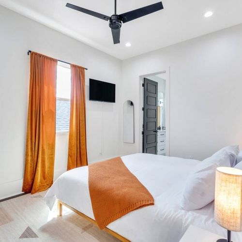 Bright bedroom w/ bold orange curtains & a warm, welcoming feel.