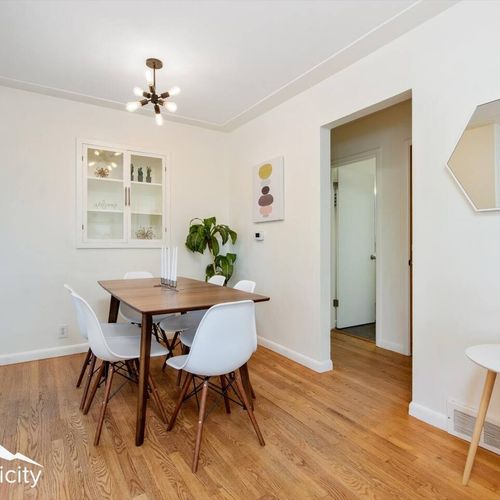 - clean lines and mid century details define this warm dining setting
- wall art, hanging light, and greenery bring a bright, curated feel
- hardwood floors and white walls create an airy space for group meals