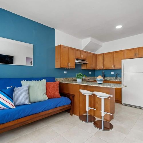 Step into a cozy, modern living space featuring a vibrant blue sofa, contrasting beautifully with the warm wooden kitchen.