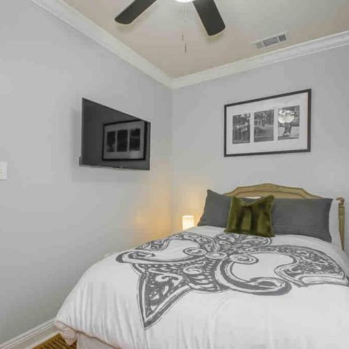 Charming bedroom w/ Fleur De Lis NOLA-themed décor, smart TV, & luggage rack.