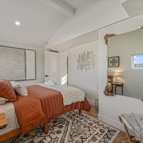 - cozy room adorned with abstract art, rustic wood nightstands, & ambient lighting - gold framed mirror reflects natural light, adding charm & a spacious feel to the room
