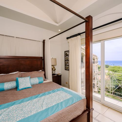Master bedroom with tropical hardwood four-poster canopy king bed, tray ceiling fan, and sliding door to Tamarindo ocean view.