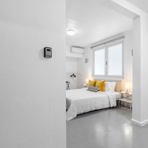 Entrada amplia y luminosa a un dormitorio sencillo con paredes y ropa de cama blancas y limpias.