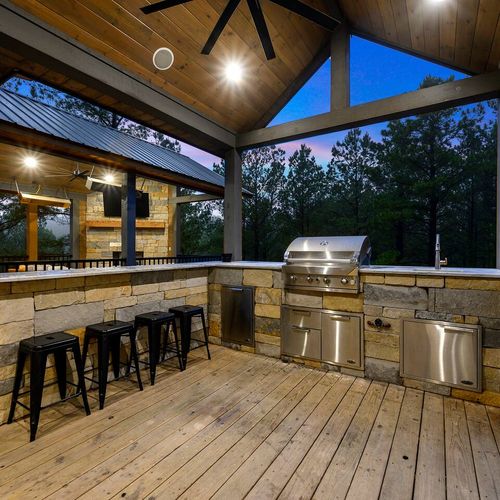 Outdoor kitchen with gas grill, bar top seating and mini fridge.