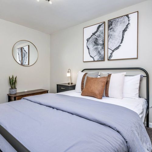 - serene bedroom with neutral color palette and soft layered bedding
- matching nightstands modern lamps and wall art complete the space
- decorative touches like a round mirror and greenery add charm and warmth