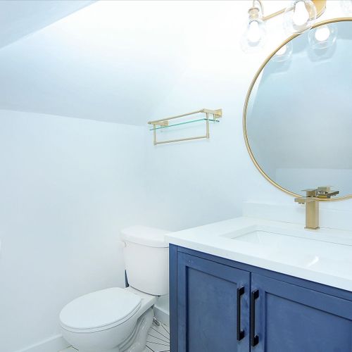 The upstairs half bath is bright and sophisticated. It has a vanity, sink, toilet and large round mirror.