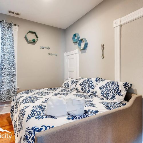 - serene bedroom retreat with a neutral headboard, blue floral bedding, and modern wall art
- matching curtain and honeycomb wall shelves add cohesion and charm
- hardwood floors and soft lighting provide a cozy restful atmosphere