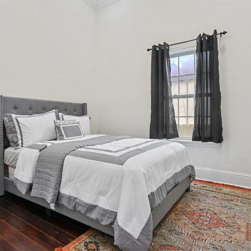 Cozy bedroom w/ a neatly made bed & natural light streaming through the curtains.