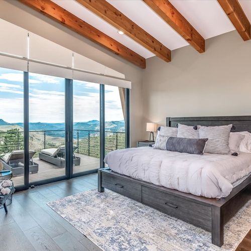 - wake up to panoramic views from this elegant bedroom with glass wall and balcony
- king bed with storage drawers and exposed beams adds comfort and charm
- step outside to enjoy mountain air and uninterrupted sunrise scenery