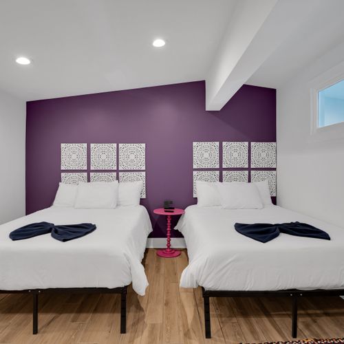 Bedroom 2 w/ twin beds, purple walls & warm wood floors for a cozy, stylish sleep.