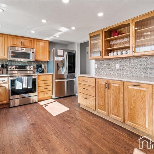 - open kitchen layout with stainless appliances, sleek backsplash, and extra cabinetry
- glass front upper cabinets make it easy to spot glassware and serving essentials
- hardwood floors and soft lighting create a warm and functional cooking space