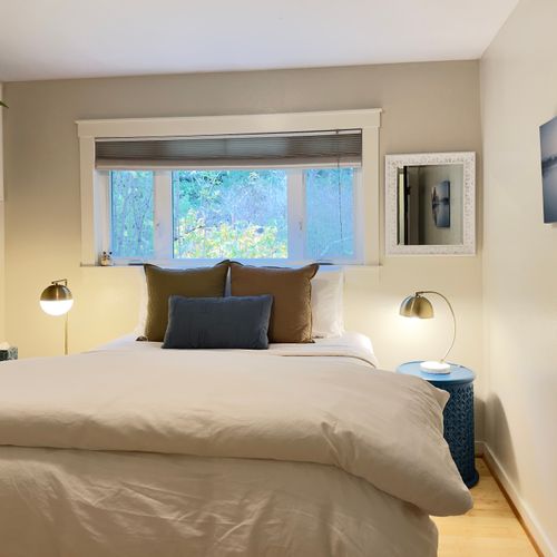 Settle into a cozy bed with soft linens and warm bedside lighting, perfect for reading or unwinding. This calm bedroom features forest views through the window, simple décor, and a peaceful feel designed for restful nights and slow mornings.
