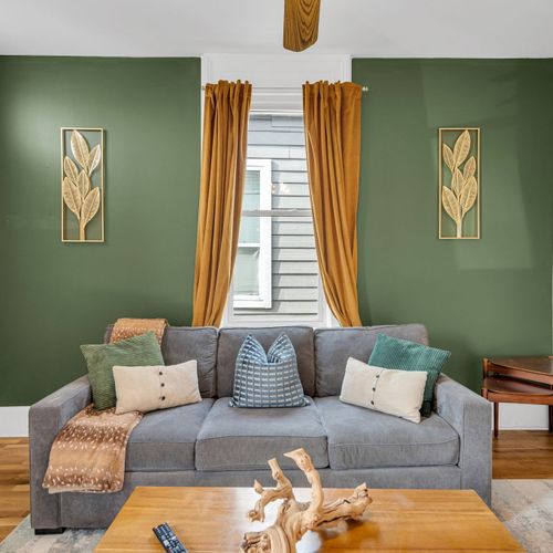 Bright living room w/ cozy seating, warm gold curtains & layered pillows for a welcoming vibe.