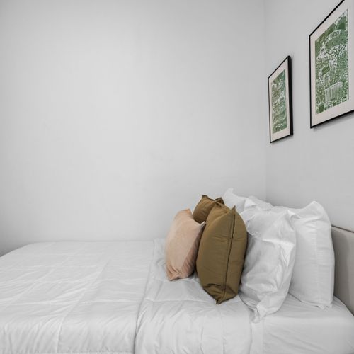 Nuestro acogedor espacio cuenta con una cama bien hecha, paredes blancas y un toque de estilo artístico con obras de arte enmarcadas con temas verdes.