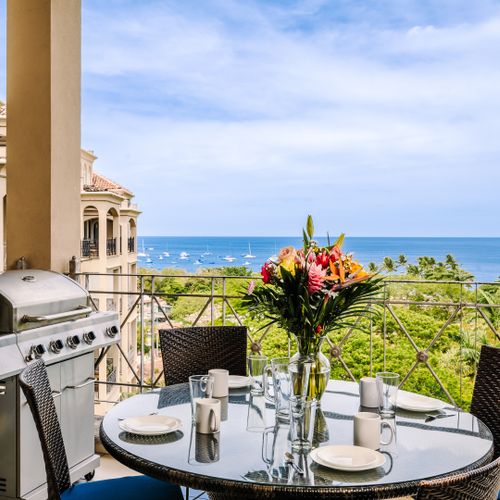 Balcony dining table with tropical flower centerpiece and sailboats anchored in Tamarindo Bay beyond.