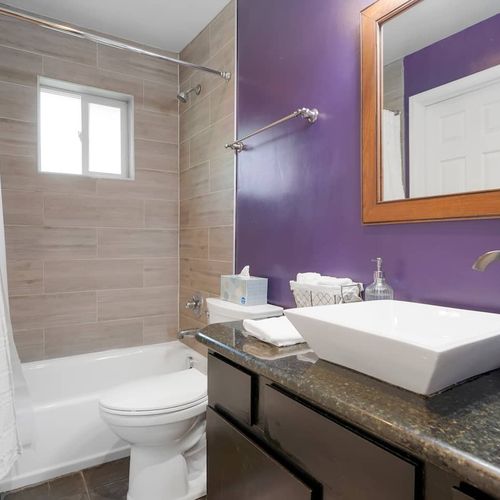 - stylish full bath featuring a vessel sink, granite counter, and tiled shower
- vibrant purple accent wall adds flair to the modern, neutral palette
- functional and fresh with everything you need for a relaxing routine