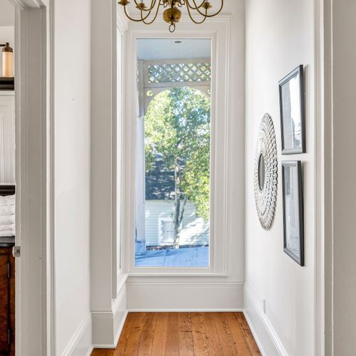 Charming hallway with hardwood floors, elegant chandelier, and a bright window offering serene outdoor views.