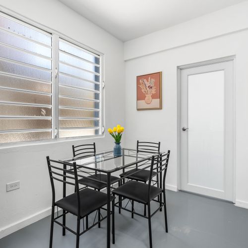 Indulge in comfort and style in this inviting dining space, complete with a sleek modern table set for four, vibrant artwork, and a cozy kitchenette.