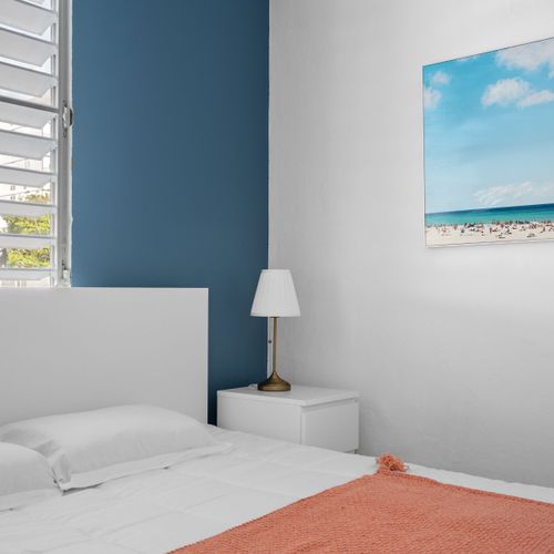 Elevate your stay with a peaceful night's sleep in this stylish bedroom adorned with minimalistic furniture and tranquil beach artwork.