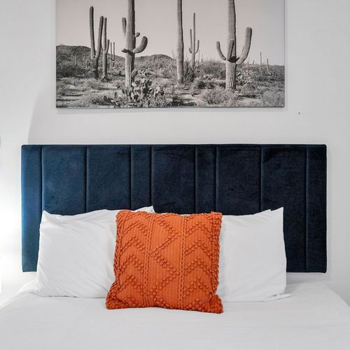 Bold bedroom w/ velvet navy headboard, orange pillows, & crisp white bedding.