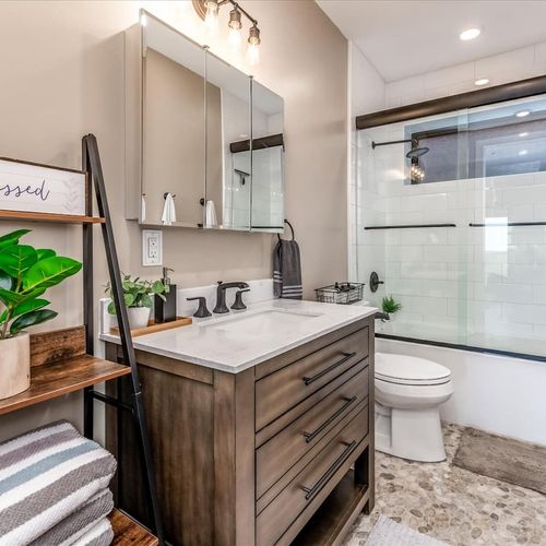 - stylish bathroom features a modern wood vanity, black hardware, and bright lighting
- sleek glass shower and pebble style flooring create a spa like touch
- complete with plush towels, storage shelves, and charming mountain decor