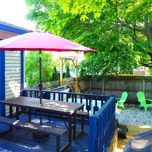 Exterior:  the fully fenced-in backyard with newly expanded deck, new hot tub, bonfire ring, propane grill, and picnic table with umbrella.