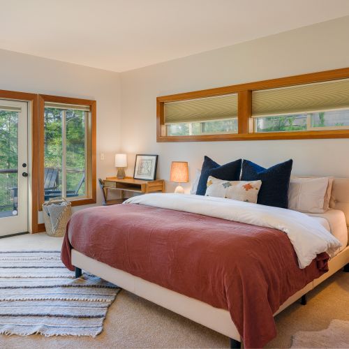 Spacious retreat with a plush king bed, warm bedside lamps, private full bathroom, and direct balcony access, plus a single couch and table for relaxing or reading.