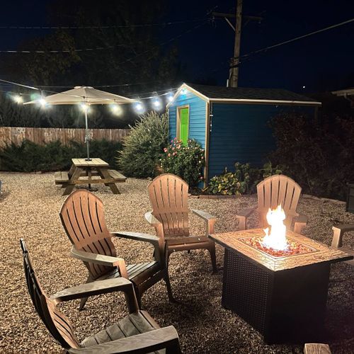 - unwind under the stars around a glowing fire pit with comfy adirondack chairs & cozy lighting
- roast marshmallows, or enjoy drinks in this inviting backyard retreat
- fun extras like cornhole, a picnic table, & a bright shed complete the laid back