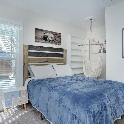- woodland themed room featuring a rustic wood headboard and peaceful animal artwork
- plush blue comforter and fluffy white pillows offer a soft, inviting sleep space
- hanging hammock chair and natural light create a relaxing reading nook