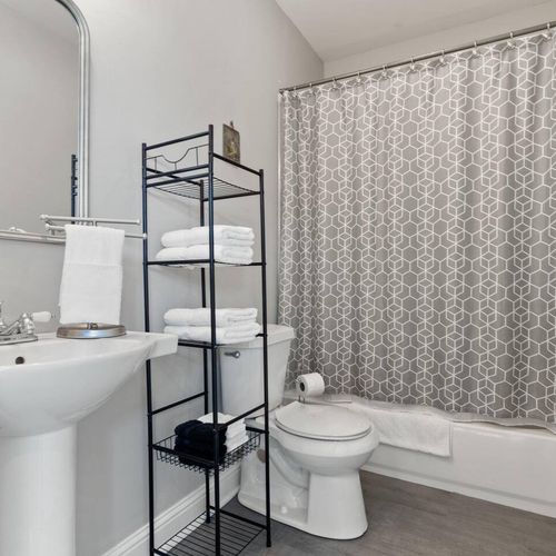 Clean bathroom w/ a tub/shower combo, toilet & handy storage shelving.