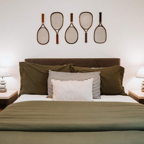 - drift off in comfort with crisp green bedding and plush pillows in this cozy nook
- unique vintage racket art adds character and charm to your restful retreat
- soft bedside lighting sets the perfect mood for winding down in style