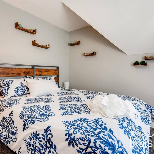 - queen bed with rustic wood headboard and navy accents sets a relaxed and stylish tone
- unique wooden shelves offer playful decor under a sloped ceiling
- soft carpeting underfoot makes this space extra warm and comfortable