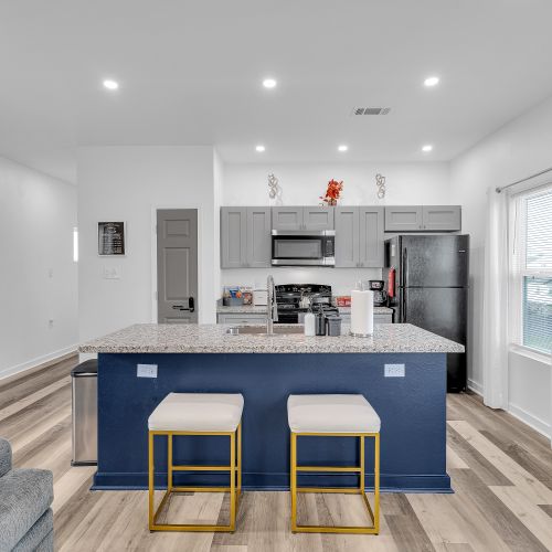 Gather around the stylish kitchen island with seating for two, perfect for morning coffee or evening conversations. Featuring sleek gray cabinetry and vibrant decor accents, this kitchen is fully equipped to meet all your culinary needs