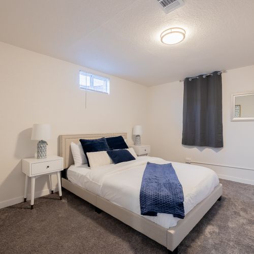 The first bedroom downstairs includes a queen size bed, black out curtains, and nightstands. Luggage racks and shelves are available for your belongings.