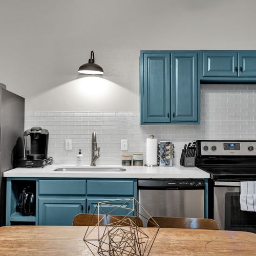 Stylish kitchen w/ bold teal cabinets, open shelving & modern appliances.
