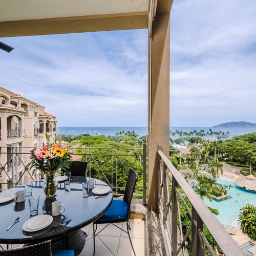 Balcony dining table with fresh flowers overlooking a free-form resort pool and Tamarindo Bay beyond.