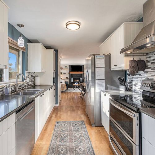 - sleek galley kitchen with stainless steel appliances, mosaic tile backsplash, and bright light
- plenty of counter space and modern fixtures make meal prep effortless
- look straight through to the cozy fireplace for open concept charm