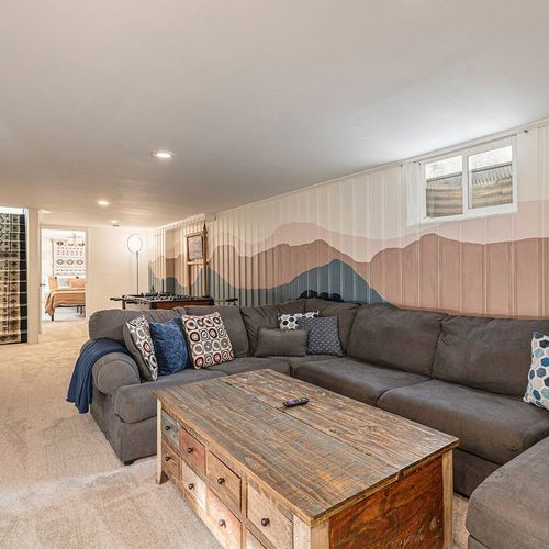 - plush sectional sofa wraps around a rustic coffee table in this basement lounge
- hand painted mountain mural adds a creative local flair to the space
- relax, binge a show, or enjoy quality time with family or friends