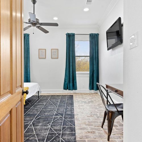 Bedroom 1 entrance w/ charming brick floors & teal curtains that set a bold, cozy tone.