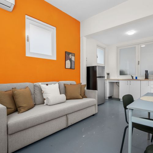 Contemporary living space offering a sleek sofa, coffee table, chairs, and a wall-mounted flat-screen TV.