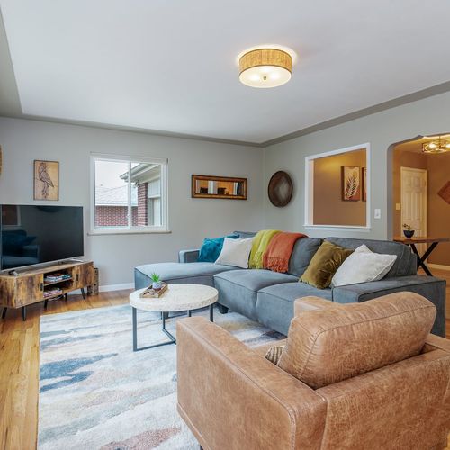- cozy living room with a spacious sectional, colorful pillows, & a modern rustic vibe
- enjoy movie nights on the flat screen tv with natural light streaming through windows
- charming touches like a window nook, woven art, &  wood accents add warm