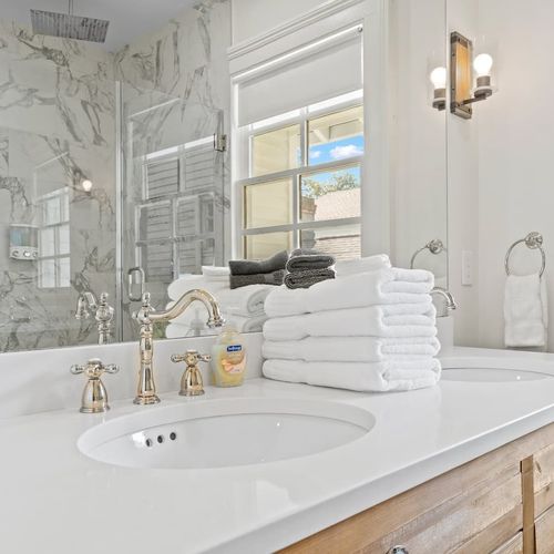 Bright bathroom vanity w/ sink, gold fixtures & neatly folded fresh towels.