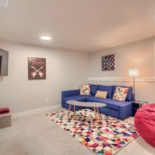 - colorful game room with bright area rug, plush blue sectional, and fun wall art