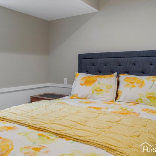 Bedroom 2 features a bright and cheerful ambiance with a queen bed and lively yellow accents, creating a welcoming and vibrant space.
