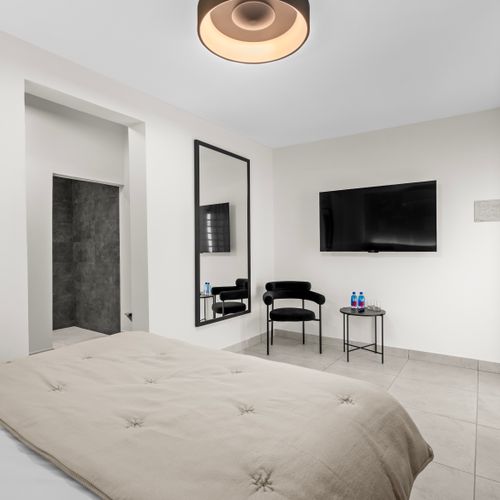 Spacious hotel room with a comfortable queen-sized bed, a large flat-screen TV, and a full-length mirror. The room features a minimalist design with neutral colors and clean lines.