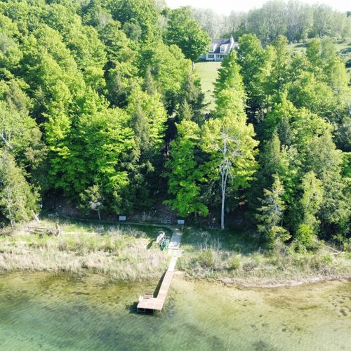 Overall:  an aerial photo from out over the lake showing the private lakefront, dock, kayaks, and canoe with the house in the background.