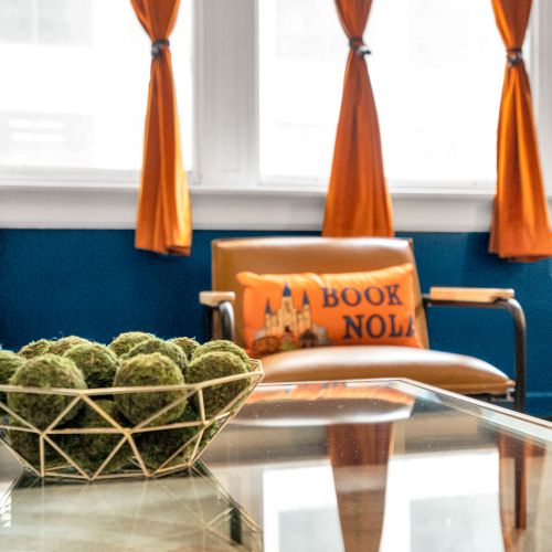 Bright, bold, and welcoming—our cozy seating area invites you to relax and soak in the New Orleans vibe, complete with our signature 'Book NOLA' pillow and a touch of local flair.