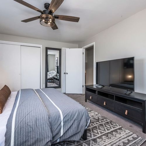 - modern bedroom with dark wood dresser large tv and full length mirror
- textured rug and ceiling fan add comfort and style to the restful layout
- plenty of closet space and calming tones make this room feel clean and inviting